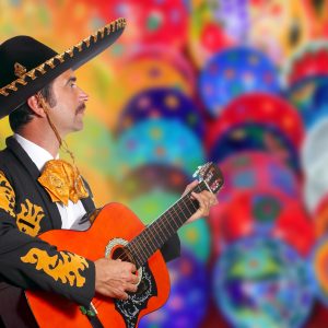 Charro Mariachi playing guitar over colorful blur handcrafts background